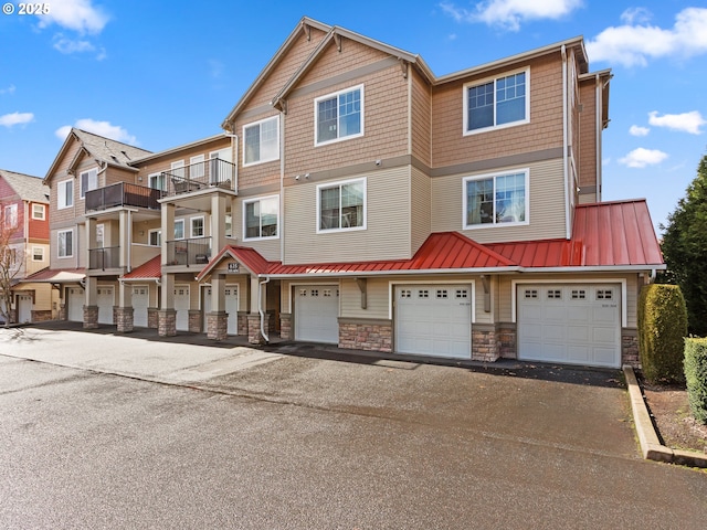 townhome / multi-family property featuring driveway, stone siding, an attached garage, a standing seam roof, and metal roof