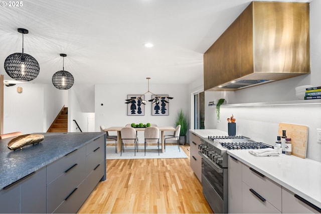 kitchen featuring gray cabinetry, decorative light fixtures, stainless steel stove, and wall chimney exhaust hood