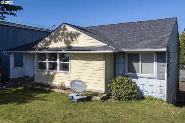 view of side of property featuring a shingled roof and a yard