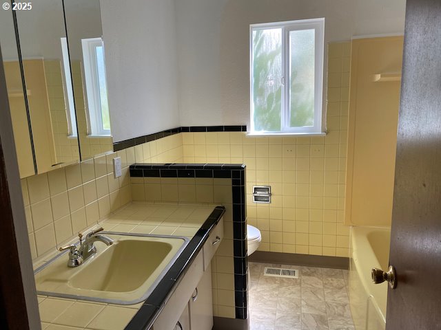 full bathroom featuring vanity, visible vents, a tub, tile walls, and toilet