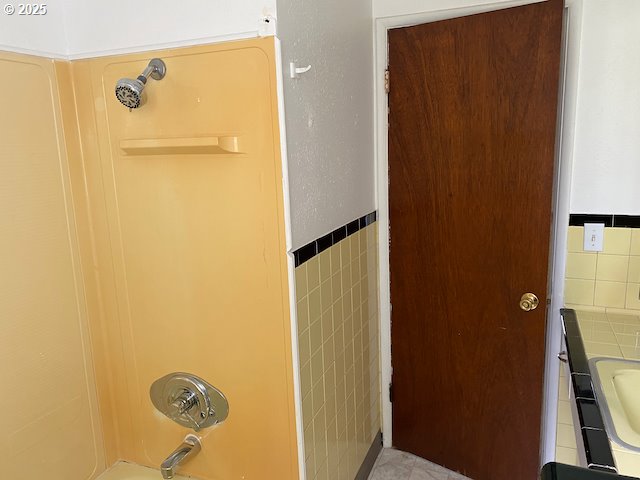 full bathroom with a sink, a wainscoted wall, tile walls, and bathtub / shower combination