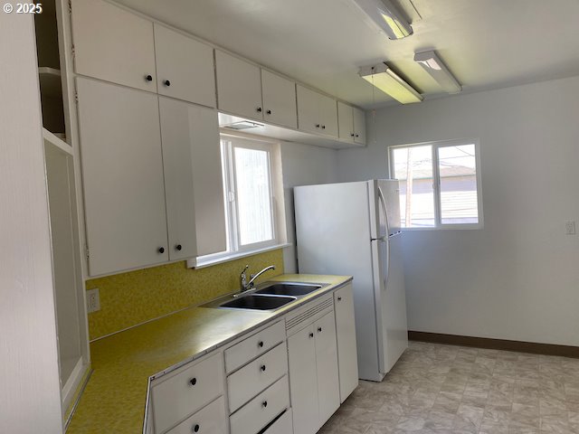 kitchen with baseboards, freestanding refrigerator, a sink, light countertops, and white cabinets