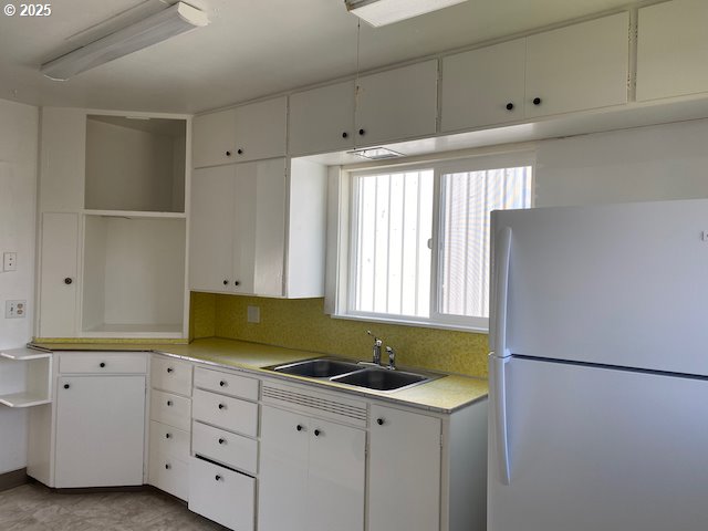 kitchen featuring open shelves, freestanding refrigerator, a sink, light countertops, and white cabinetry