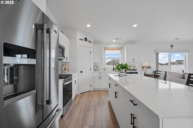 kitchen with light wood finished floors, stainless steel appliances, white cabinetry, light countertops, and a kitchen island
