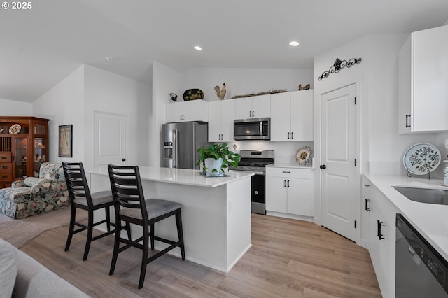 kitchen featuring light wood-style flooring, a kitchen bar, lofted ceiling, a kitchen island, and appliances with stainless steel finishes