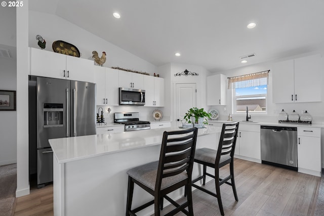 kitchen featuring white cabinets, a kitchen breakfast bar, lofted ceiling, light countertops, and appliances with stainless steel finishes