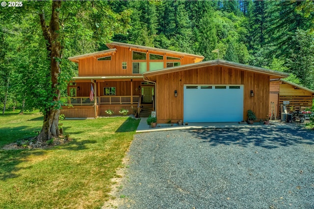 view of front of home with a front yard, gravel driveway, covered porch, and an attached garage