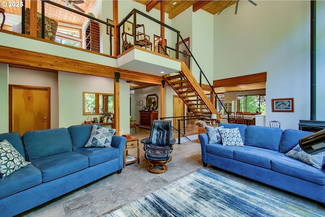 living room featuring beam ceiling, stairs, a wood stove, and a high ceiling