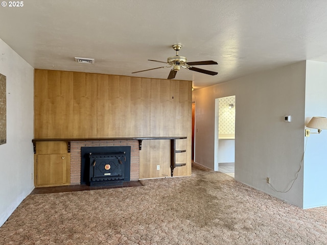 unfurnished living room featuring a fireplace, carpet floors, wooden walls, and ceiling fan