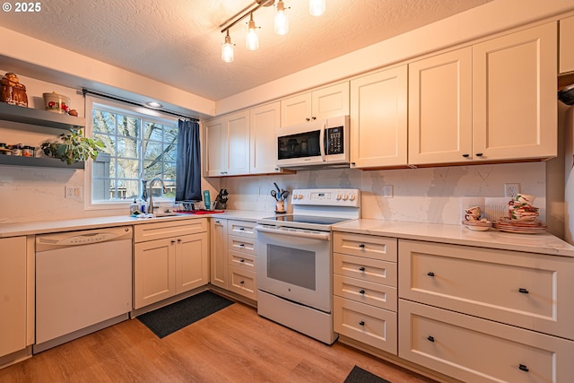 kitchen with sink, white appliances, a textured ceiling, and light hardwood / wood-style flooring