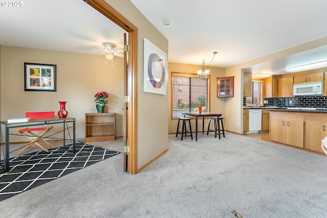 kitchen featuring light brown cabinetry, decorative backsplash, hanging light fixtures, light colored carpet, and white appliances