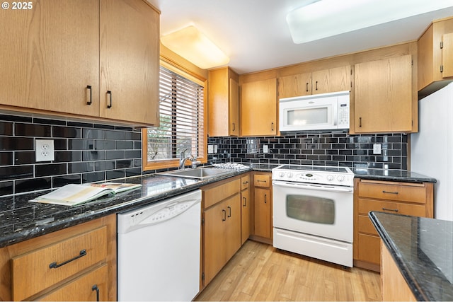 kitchen with dark stone countertops, sink, white appliances, and light wood-type flooring