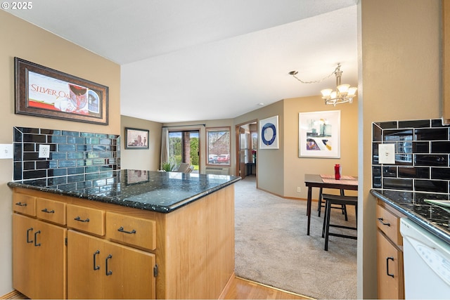 kitchen featuring dishwasher, kitchen peninsula, light carpet, decorative light fixtures, and dark stone counters