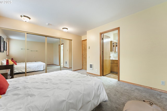 bedroom featuring a closet, ensuite bathroom, and light carpet