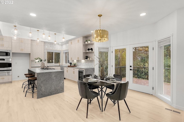 dining space featuring light wood-type flooring, a healthy amount of sunlight, a chandelier, and wine cooler