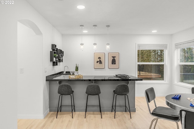 kitchen with a kitchen bar, kitchen peninsula, light hardwood / wood-style flooring, hanging light fixtures, and sink