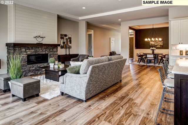 living room with a notable chandelier, light wood-type flooring, and a stone fireplace