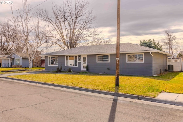 ranch-style home with central air condition unit, a shingled roof, a yard, and fence