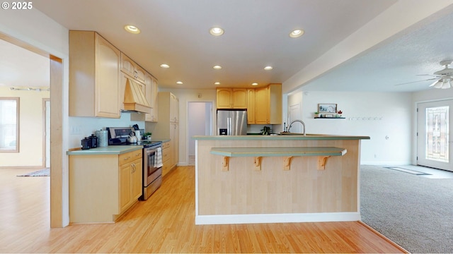 kitchen with light brown cabinetry, custom range hood, a kitchen breakfast bar, recessed lighting, and appliances with stainless steel finishes