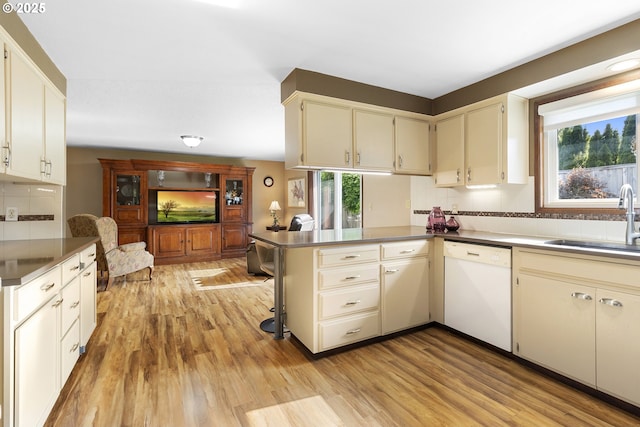 kitchen with dishwasher, a sink, backsplash, light wood-type flooring, and a peninsula