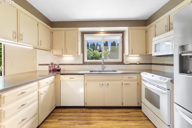 kitchen with white appliances, a sink, tasteful backsplash, light wood finished floors, and cream cabinetry