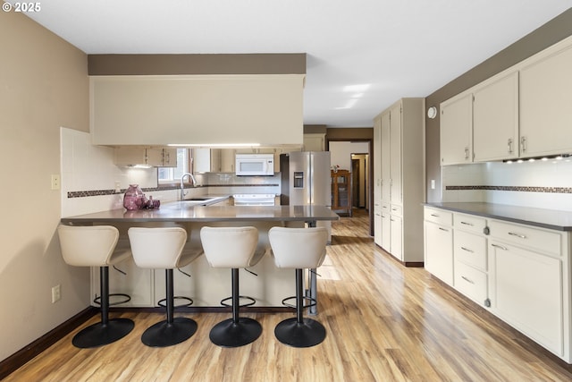 kitchen featuring white microwave, stainless steel refrigerator with ice dispenser, light wood-style flooring, and tasteful backsplash