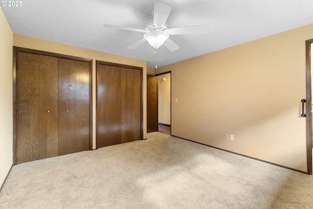 unfurnished bedroom featuring carpet floors, two closets, baseboards, and ceiling fan