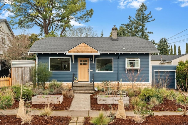 bungalow-style house with a garden, a shingled roof, a chimney, and fence