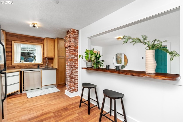 kitchen featuring light wood finished floors, a kitchen bar, appliances with stainless steel finishes, a textured ceiling, and a sink