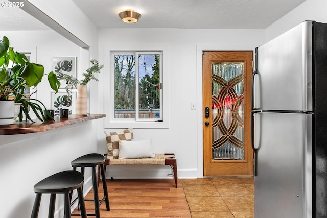 kitchen with light wood finished floors, a breakfast bar area, freestanding refrigerator, and baseboards