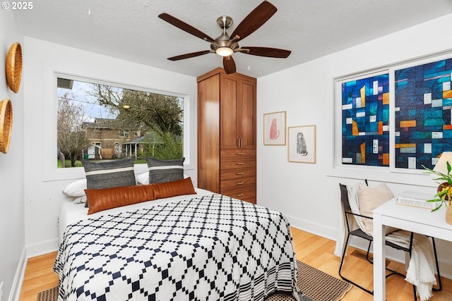 bedroom featuring visible vents, baseboards, ceiling fan, light wood-style flooring, and a textured ceiling