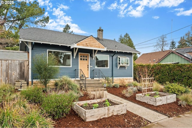 bungalow-style house with roof with shingles, a vegetable garden, a chimney, and fence