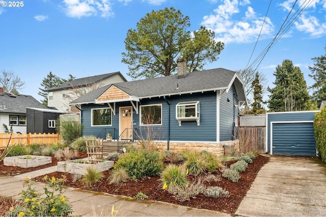 bungalow featuring fence, concrete driveway, roof with shingles, stone siding, and a vegetable garden