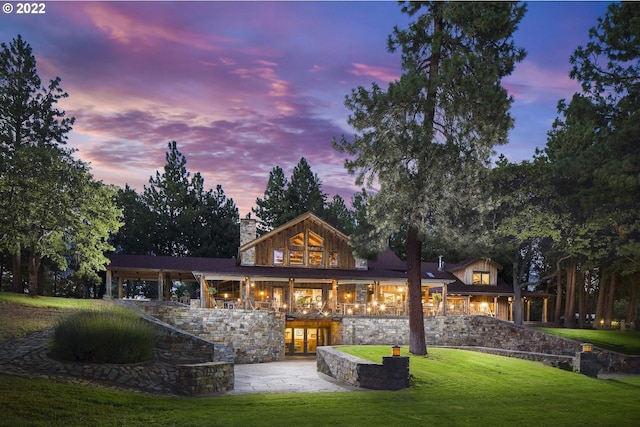 back house at dusk featuring a lawn and a patio