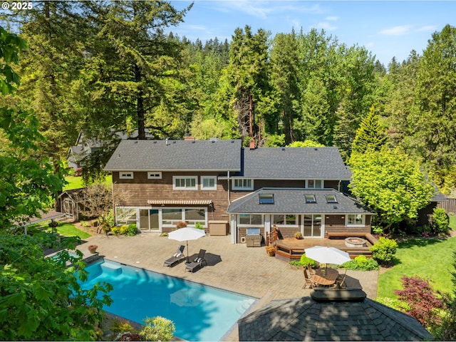 back of property featuring a wooden deck, an outdoor pool, a patio, roof with shingles, and a jacuzzi
