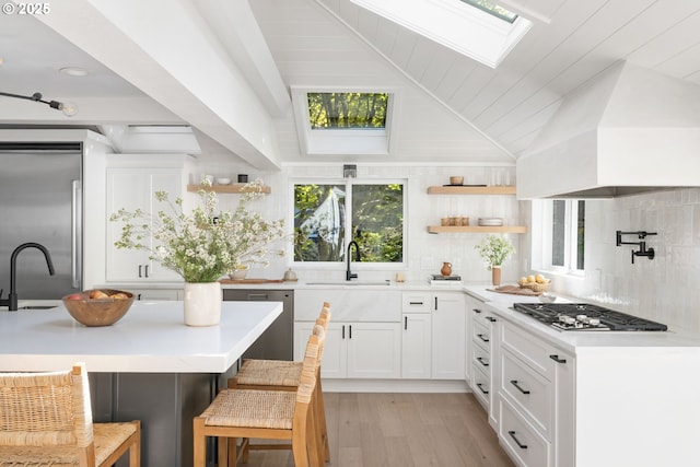 kitchen featuring open shelves, custom range hood, a sink, stainless steel appliances, and a skylight