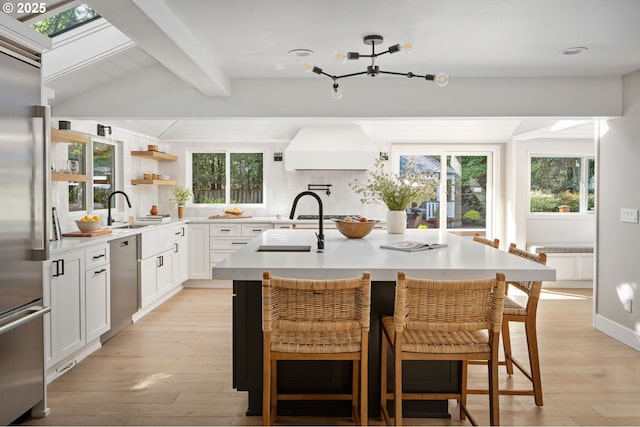 kitchen featuring appliances with stainless steel finishes, beamed ceiling, light countertops, a sink, and an island with sink