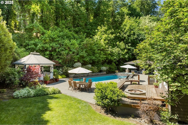 swimming pool with a gazebo, a fire pit, a patio, a lawn, and a wooden deck