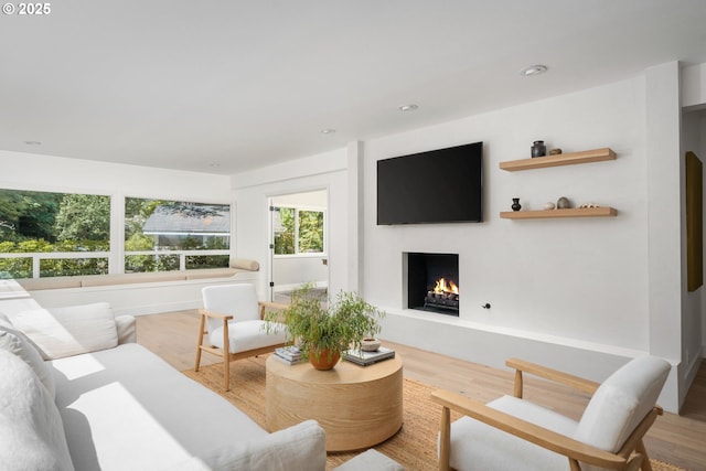 living room with a warm lit fireplace, plenty of natural light, wood finished floors, and recessed lighting