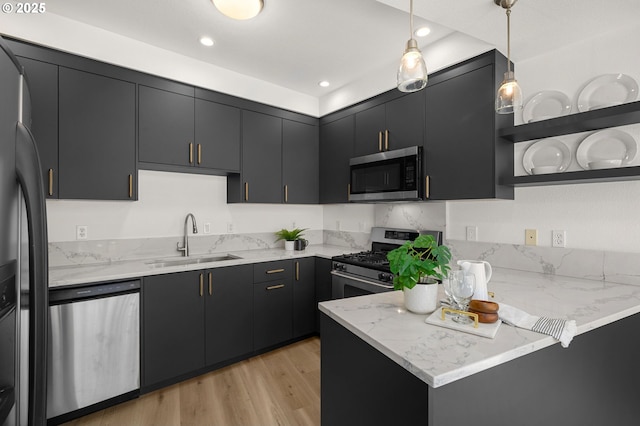 kitchen featuring light stone countertops, appliances with stainless steel finishes, light wood-type flooring, sink, and decorative light fixtures