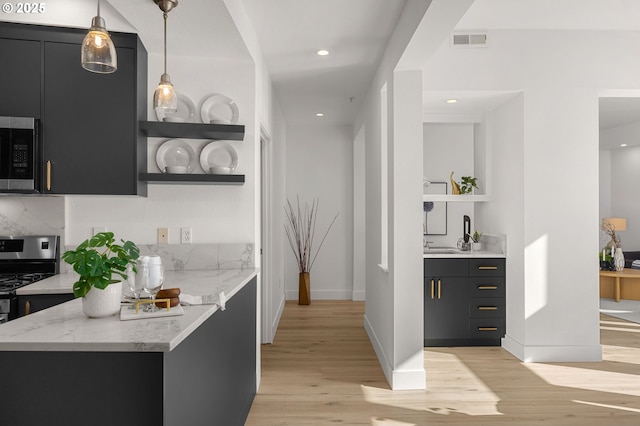 bar featuring light stone counters, decorative light fixtures, decorative backsplash, appliances with stainless steel finishes, and light wood-type flooring