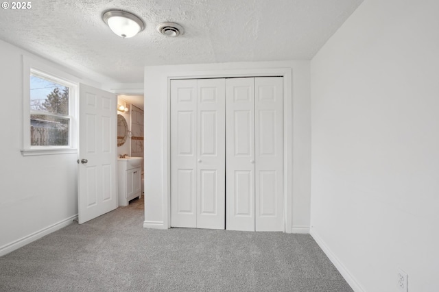 unfurnished bedroom featuring a textured ceiling, a closet, carpet, and visible vents