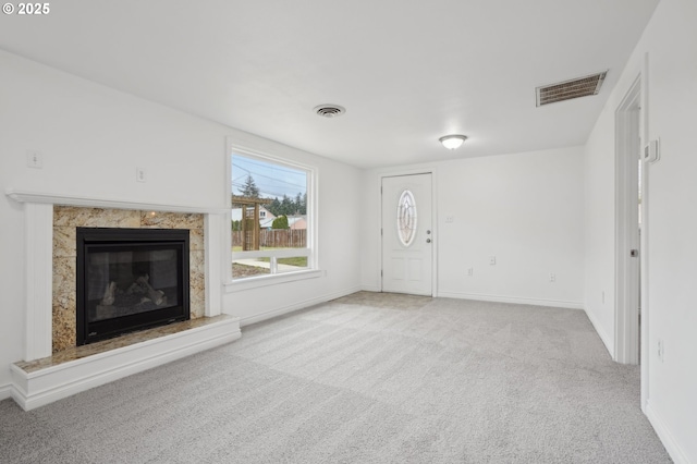 unfurnished living room with carpet, a high end fireplace, visible vents, and baseboards