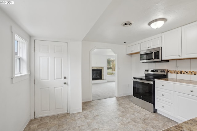 kitchen with stainless steel appliances, a glass covered fireplace, visible vents, and white cabinetry