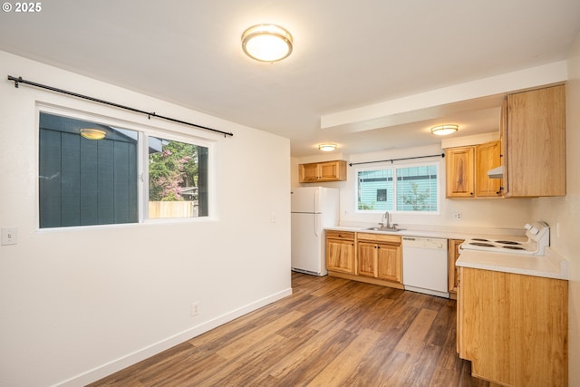 kitchen featuring a sink, white appliances, light countertops, baseboards, and wood finished floors