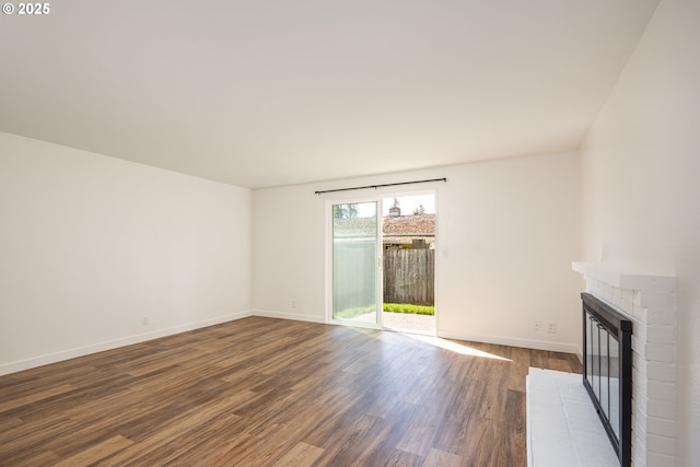 unfurnished living room featuring baseboards, dark wood finished floors, and a brick fireplace
