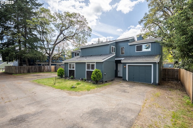 view of front facade featuring fence, driveway, a shingled roof, and a garage