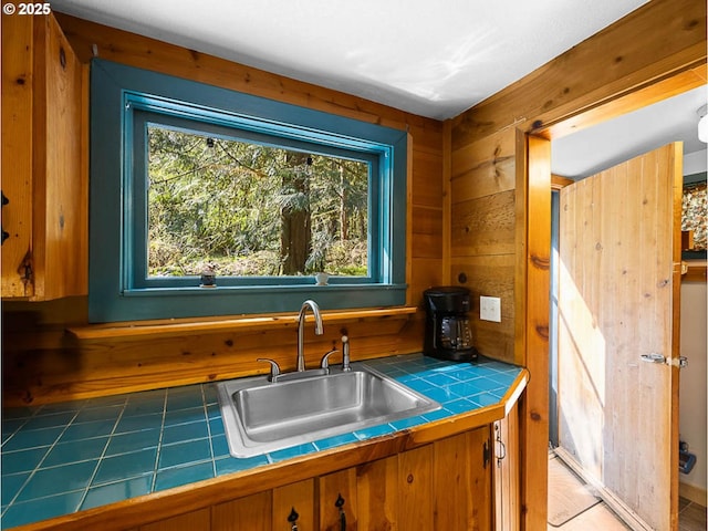 kitchen featuring wooden walls, tile counters, brown cabinetry, and a sink