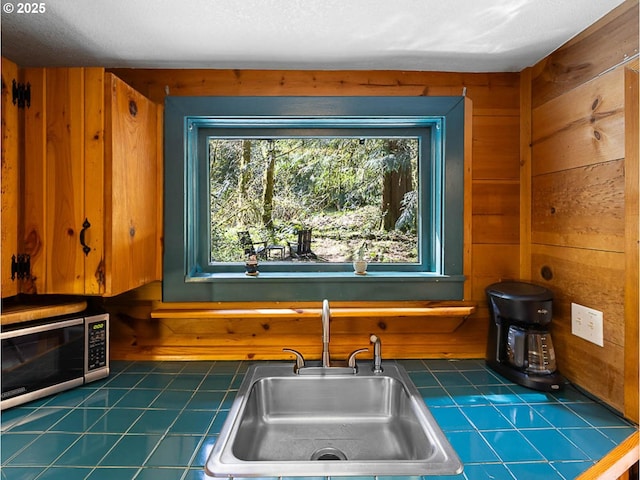 kitchen with tile counters, stainless steel microwave, wood walls, and a sink