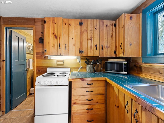 kitchen featuring white range with electric stovetop, tile counters, brown cabinetry, stainless steel microwave, and light tile patterned floors